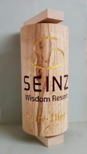 Gebetsmühle aus Lindenholz mit dem Logo des SEINZ Wisdom Resort, an der Wand montiert